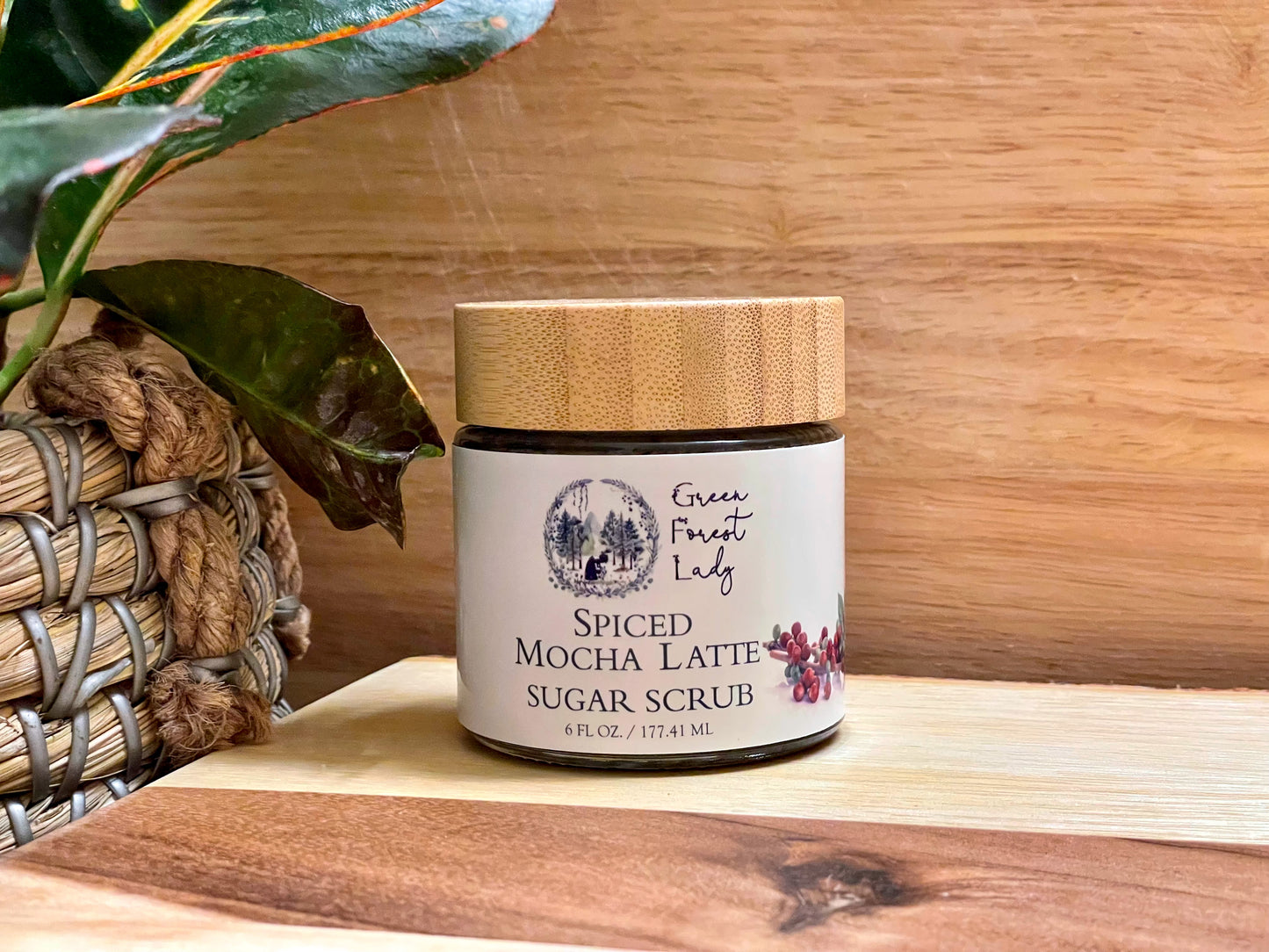 Spiced Mocha Latte Sugar Scrub in a glass jar on a wooden spa table by a plant