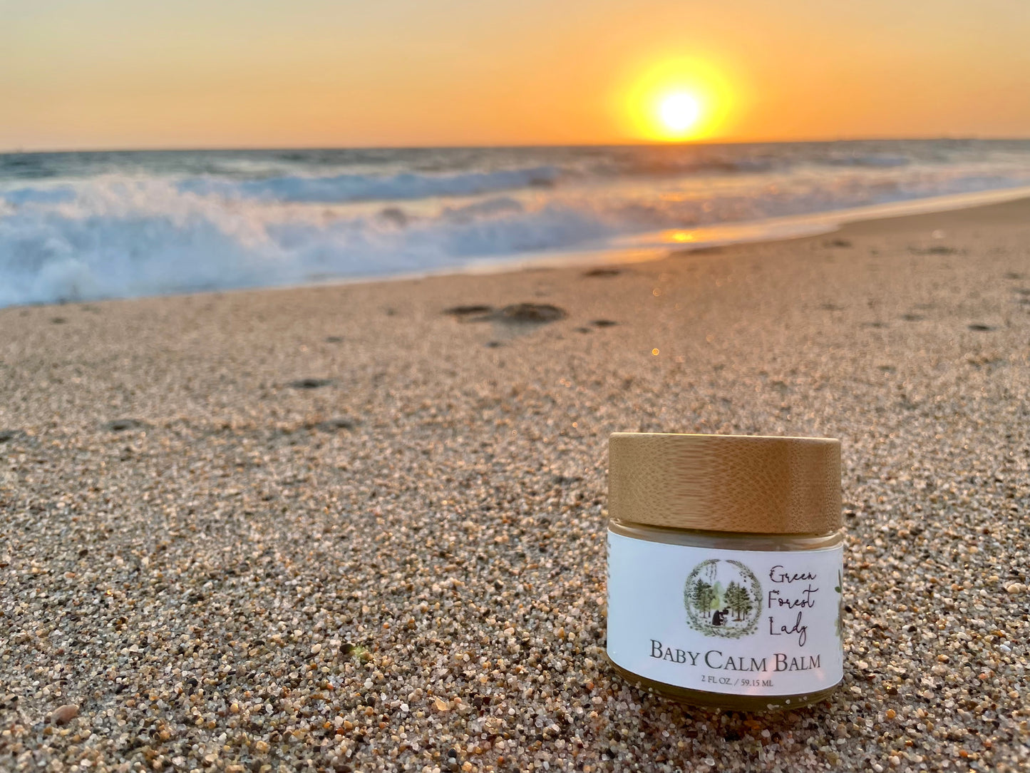 Jar of Baby Calm Balm on a beach beside an outgoing wave