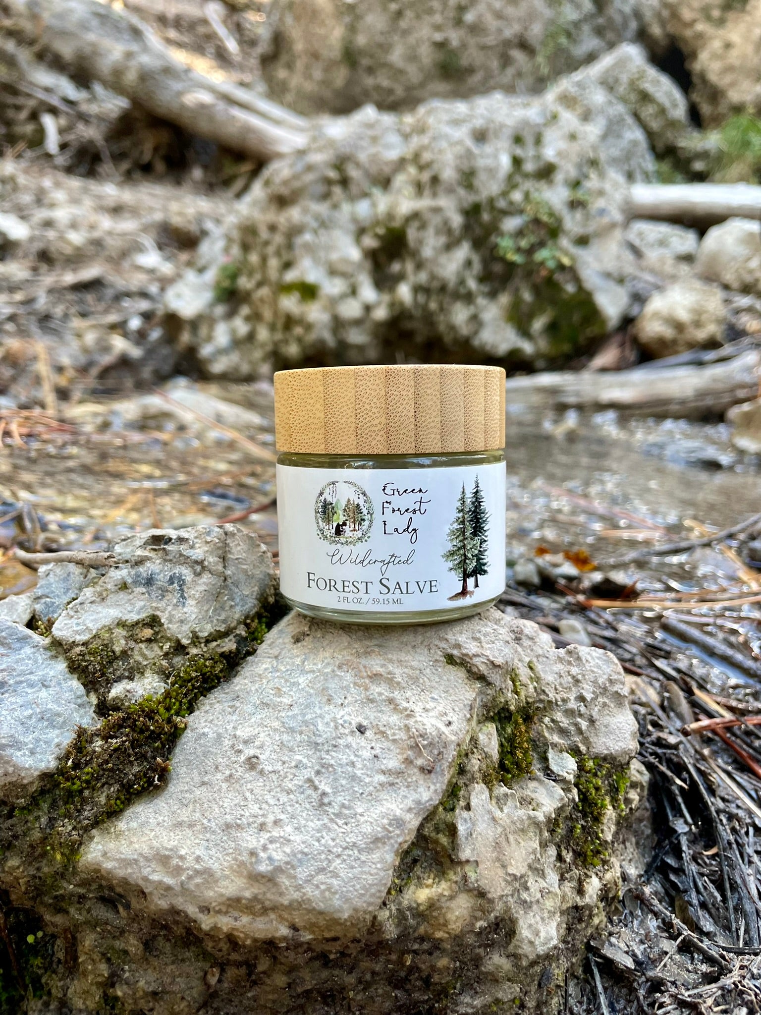 A jar of Forest Salve sitting on a large rock by a stream