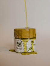 Load image into Gallery viewer, Jar of Nipple Balm with a natural ingredient pouring over it.
