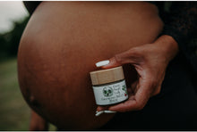 Load image into Gallery viewer, Woman with a large growing pregnant belly holding a jar of Growing Belly Balm

